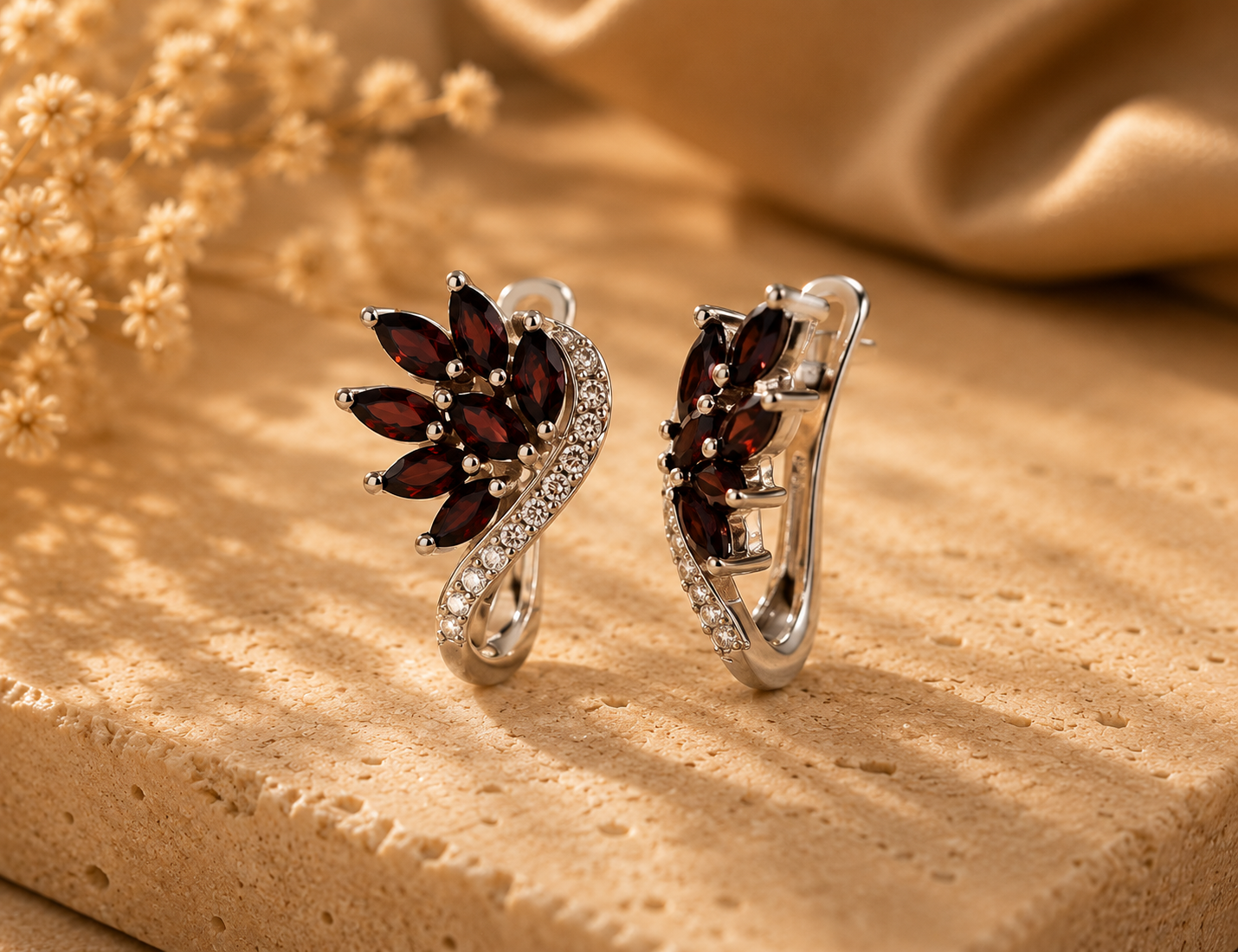 Elegant silver earrings with deep red garnet gemstones and sparkling zircon accents on a luxury beige stone background.